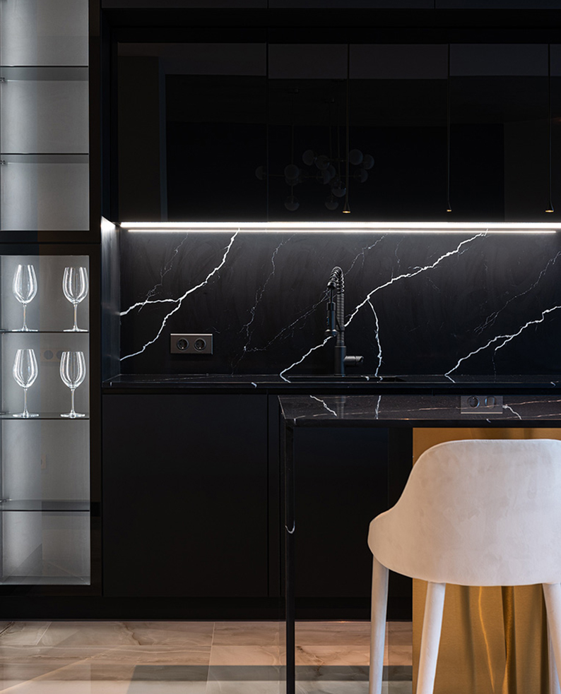 Cucina di colore nero con muro effetto marmo e profili a LED RIFT posizionati sotto pensile.