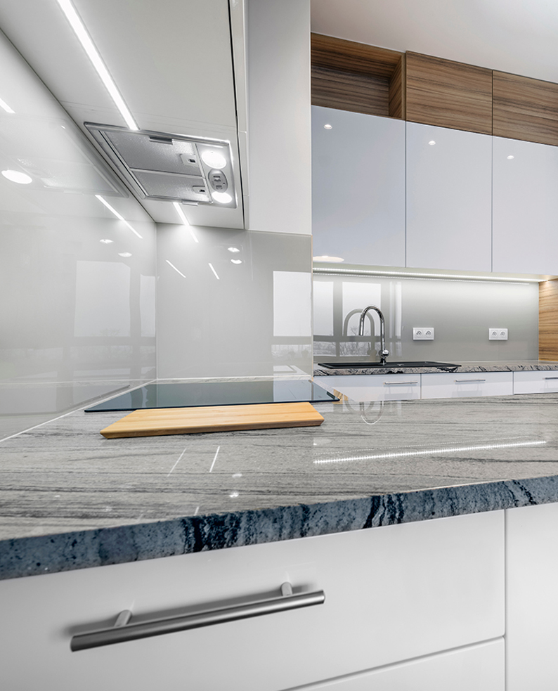 Cucina moderna bianca con top in marmo, illuminata dai profili a LED SIS posizionati sotto pensile.