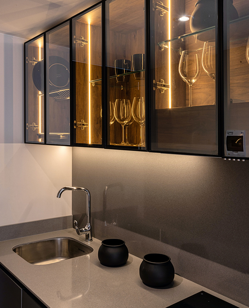 Cucina con top in marmo e pensili con ante in vetro e profili a LED incassati sui fianchi dei pensili.