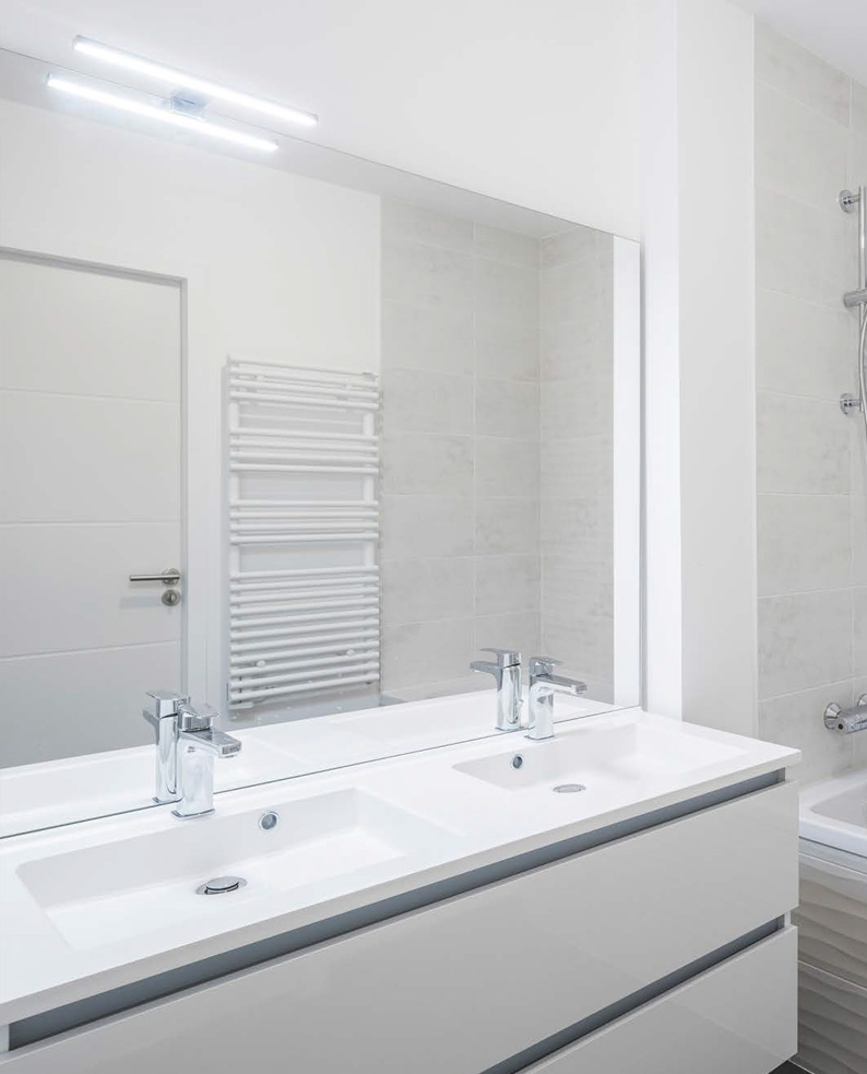 bagno moderno con arredi bianchi e illuminazione a LED POP sopra la specchiera.